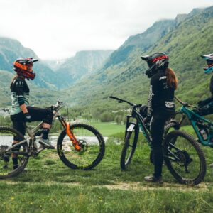 Trois vététistes équipés de protections complètes sur un sentier de montagne dans la vallée de Loudenvielle, Pyrénées, prêts à dévaler une piste de VTT enduro.